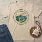 Beige cotton t-shirt with "Lead Me To The Rock And A Rescue Dog" graphic featuring mountains, sun, hiker, and dog.