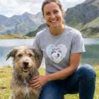 Woman in a grey Husky Heart T-shirt with a watercolor husky design, petting a shaggy dog by a lake.