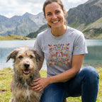 Woman in a grey Gildan Softstyle t-shirt with a colorful dachshunds and fall leaves design, kneeling beside a dog outdoors.