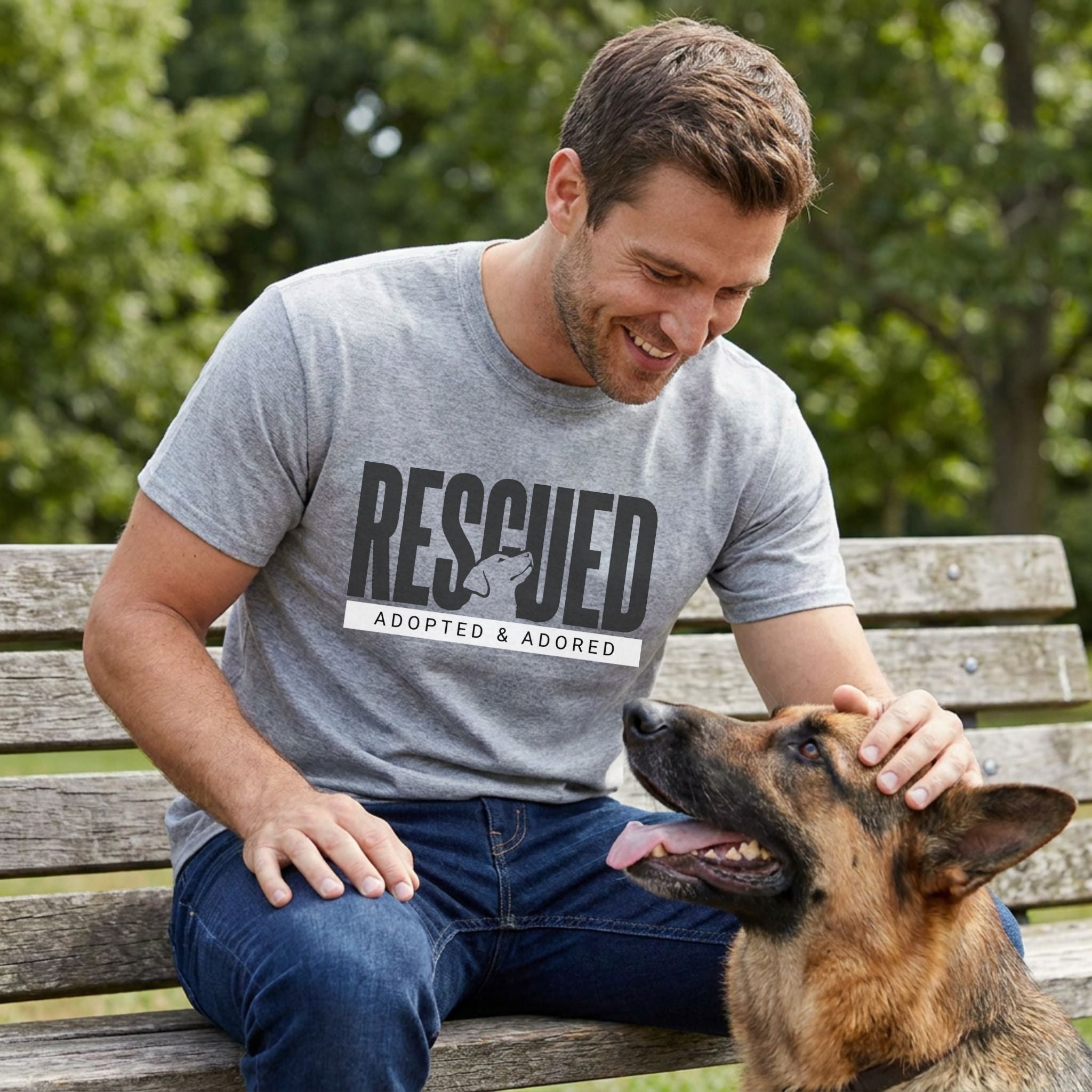Man in a grey "RESCUED ADOPTED & ADORED" t-shirt petting a German Shepherd on a park bench.