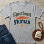 Heather gray "Emotional Support Human" t-shirt with a paw print, next to jeans and dog treats.