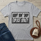 Light grey Gildan Softstyle® t-shirt with "ADOPT DON'T SHOP EXPLICIT LOYALTY" in black text, featuring paw prints.