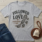 Heather gray "Followed By Love" t-shirt with a boot print and paw prints, next to jeans and dog treats.
