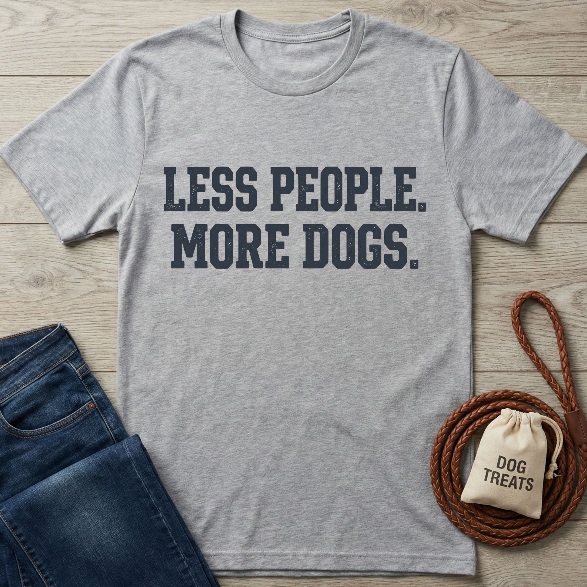 Heather gray "Less People. More Dogs." t-shirt with blue jeans and dog treats bag on wood.