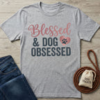 Light grey Gildan Softstyle t-shirt with "Blessed & Dog Obsessed" in pink and charcoal, featuring a paw print heart.