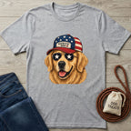 Gray t-shirt with a dog wearing an American flag cap design, paired with jeans and a dog treat bag on a wooden surface.
