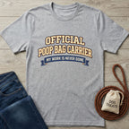 Light grey Gildan Softstyle® t-shirt with "OFFICIAL POOP BAG CARRIER" text, next to jeans and dog treats.