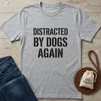 Light grey Gildan Softstyle t-shirt with "DISTRACTED BY DOGS AGAIN" in black text, next to jeans and dog treats.