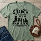 Sage green cotton t-shirt with "Official Shadow Management Team" graphic featuring a person and five dogs.
