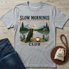Grey crewneck t-shirt featuring a dog and coffee mug on a dock overlooking a lake, mountains, and sunrise.