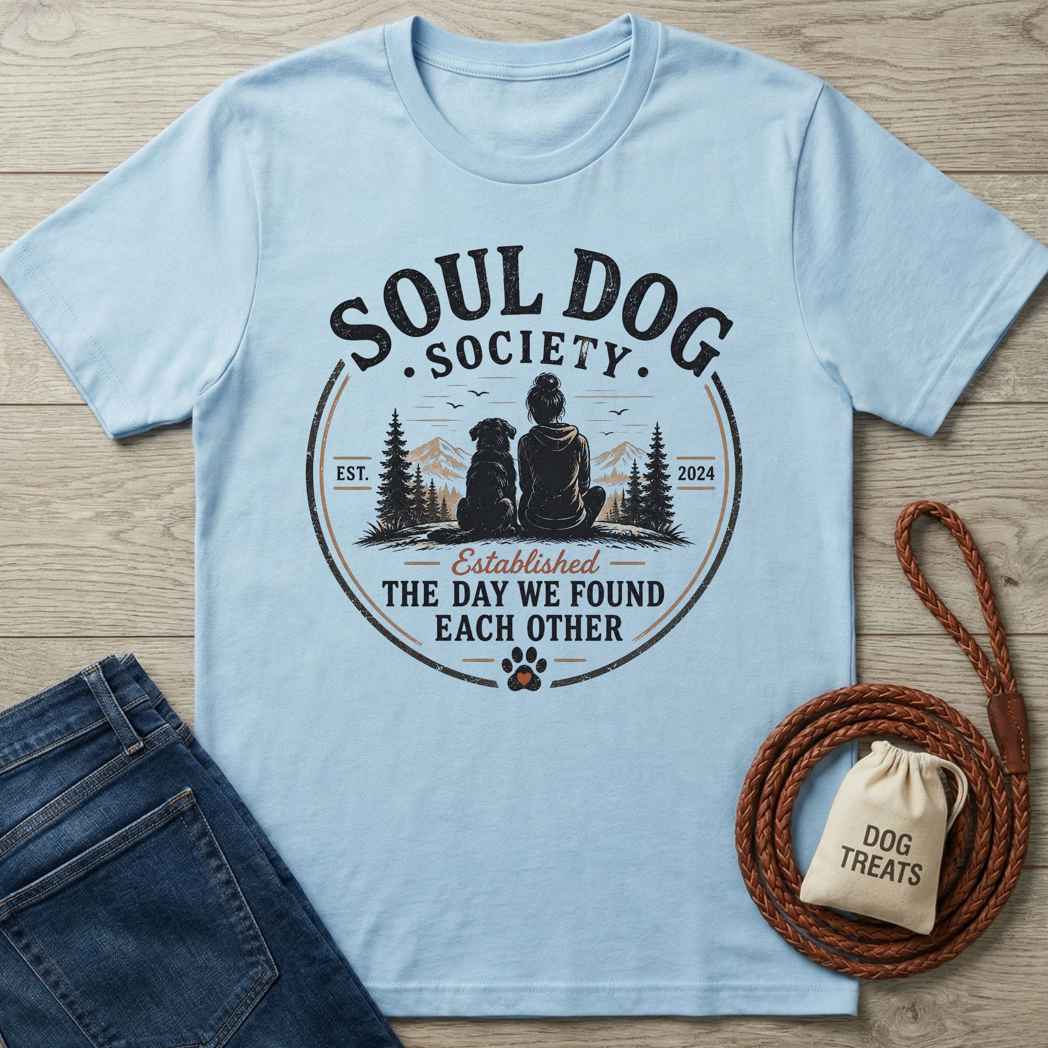Light blue Gildan Softstyle® t-shirt with "Soul Dog Society" graphic of a person and dog, next to jeans and dog leash.