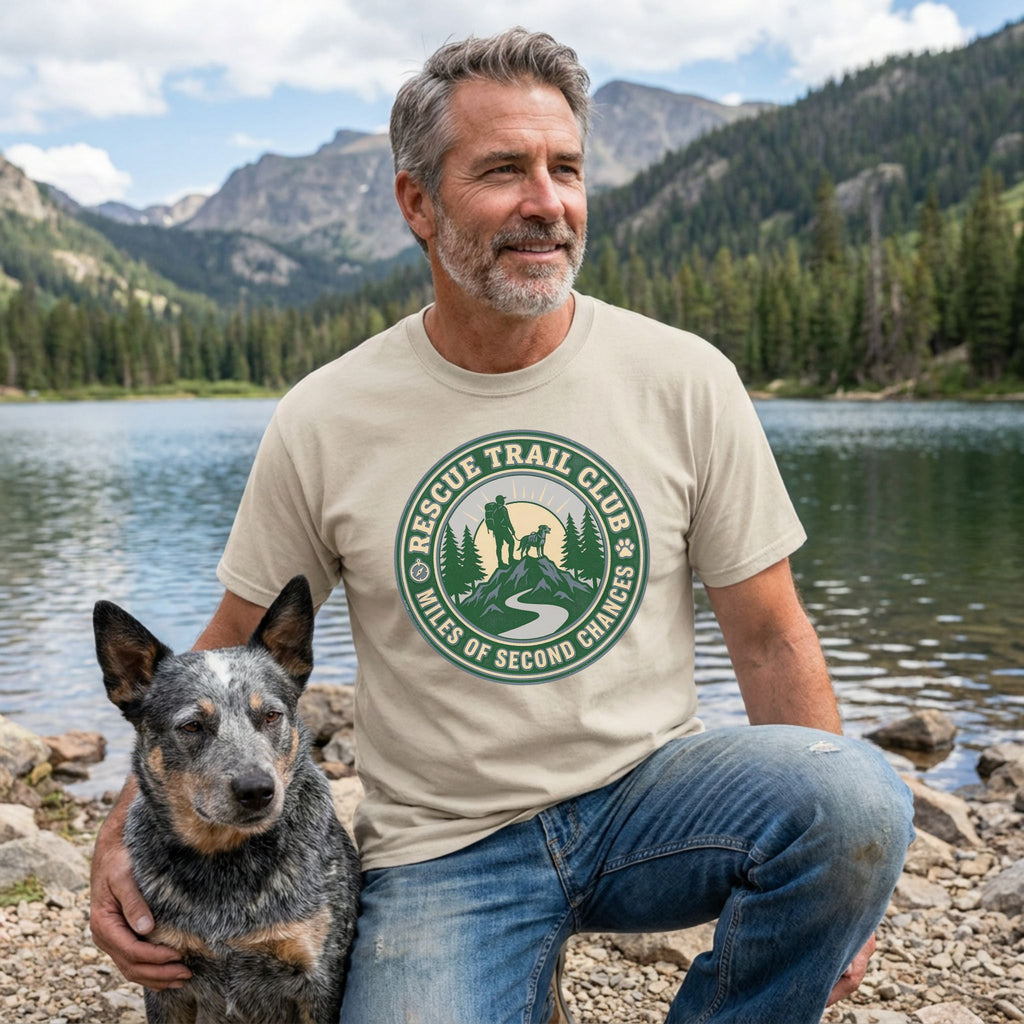 Man in a beige "Rescue Trail Club" tee with a dog, mountains, and lake in the background.
