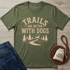 Olive green "Trails Are Better With Dogs" T-shirt with a mountain, trees, and dog design, next to jeans and dog treats.