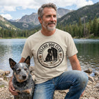 Man wearing a beige crewneck t-shirt with a Velcro Dog Club graphic featuring a dog sitting by a person's legs.