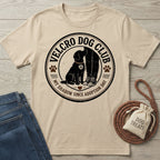 Beige crewneck t-shirt featuring a black circular graphic of a dog sitting by a person's legs with Velcro Dog Club text.