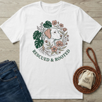 White cotton t-shirt with "Rescued & Rooted" design featuring a dog, monstera leaves, and pink flowers.