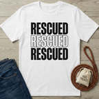 White cotton "Rescued" t-shirt with bold black text, next to blue jeans, a braided leash, and a "Dog Treats" bag.