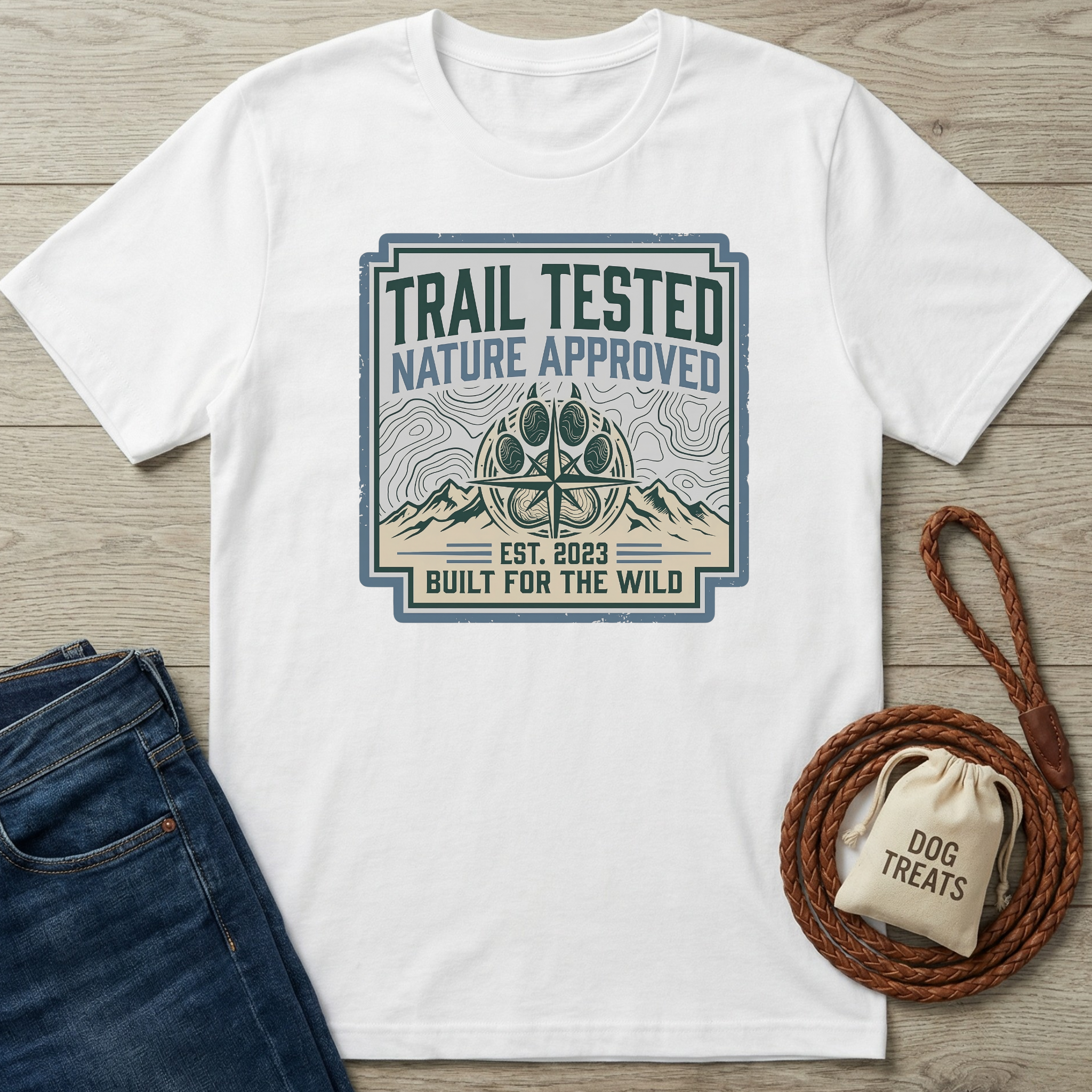 White t-shirt with 'Trail Tested, Nature Approved' design on a wooden surface with jeans and a dog leash.