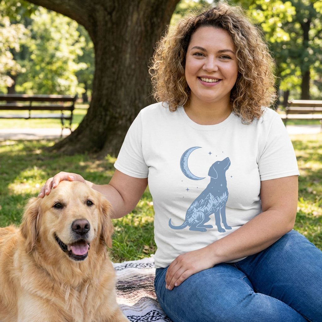 Woman in white t-shirt with blue moonlit dog and mountain silhouette design, petting a golden retriever.