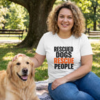 Woman in white "Rescued Dogs Rescue People" tee, petting a golden retriever in a park.