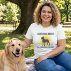 Woman in a white "Sent From Above" t-shirt with a dog graphic, petting a golden retriever in a park.