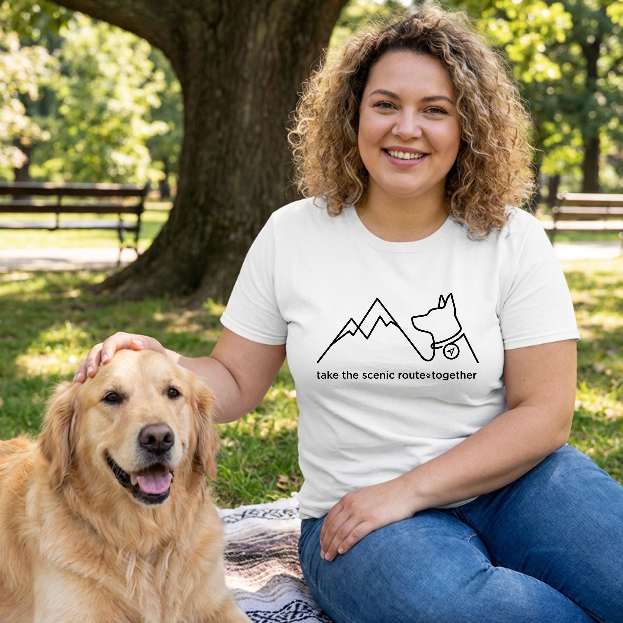 Woman in white "Take The Scenic Route Together" tee with mountain and dog design, petting a golden retriever.