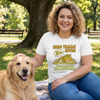 Woman in white "Zero Trails Given" t-shirt with sleeping dog graphic, petting a golden retriever in a park.