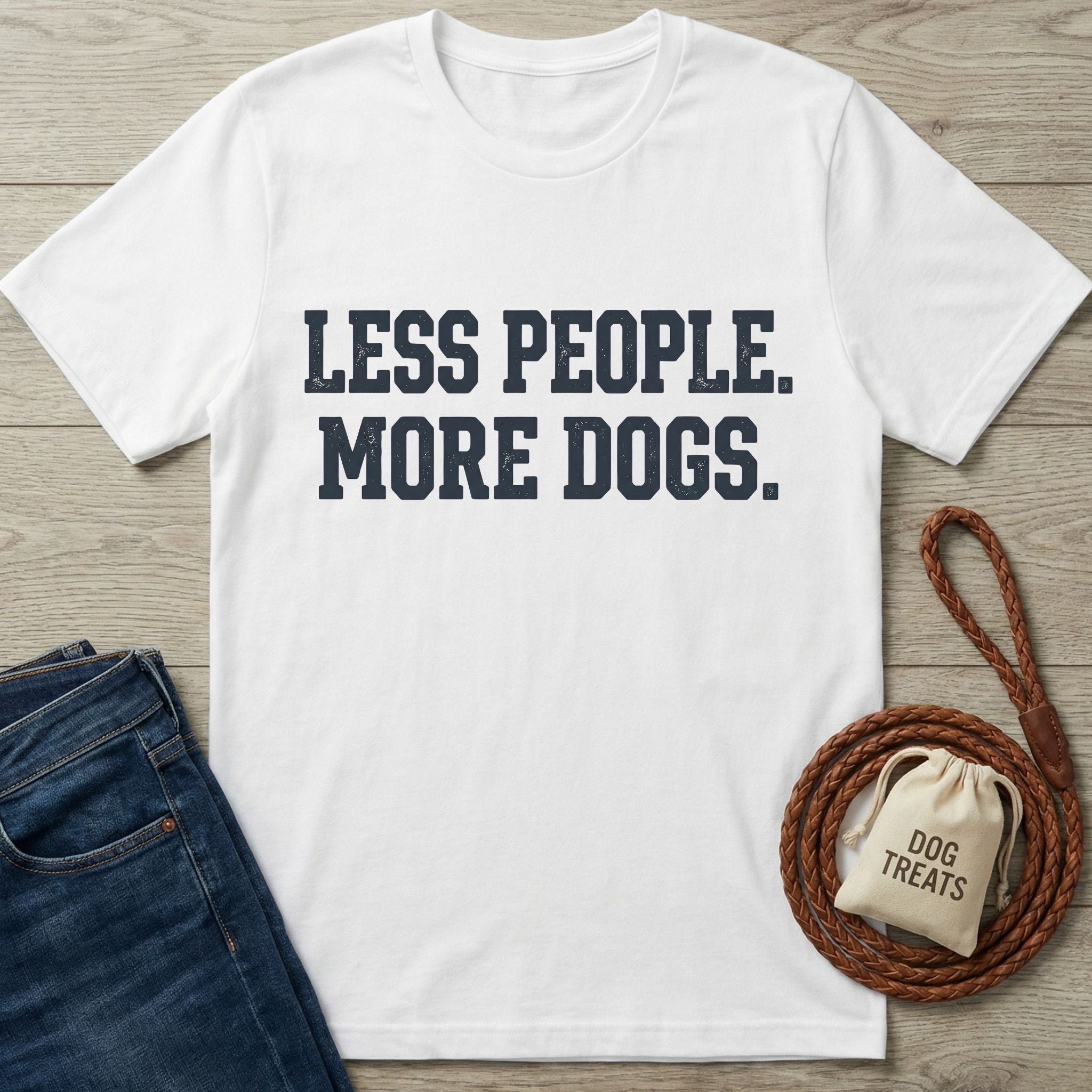 White cotton t-shirt with "LESS PEOPLE. MORE DOGS." in distressed navy text, beside jeans and a dog leash.